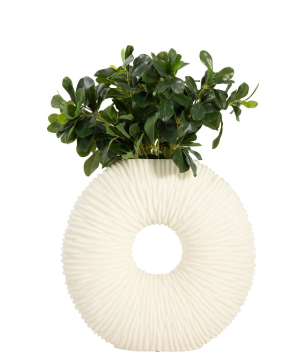 Round ivory vase with a hole in the middle and textured surface, with green foliage, on a white background. 