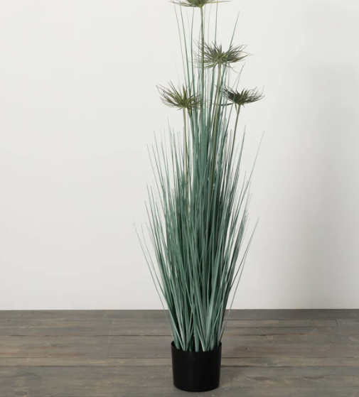 A potted artificial grass plant with lush green leaves and delicate bursting blooms, placed in a black pot.
