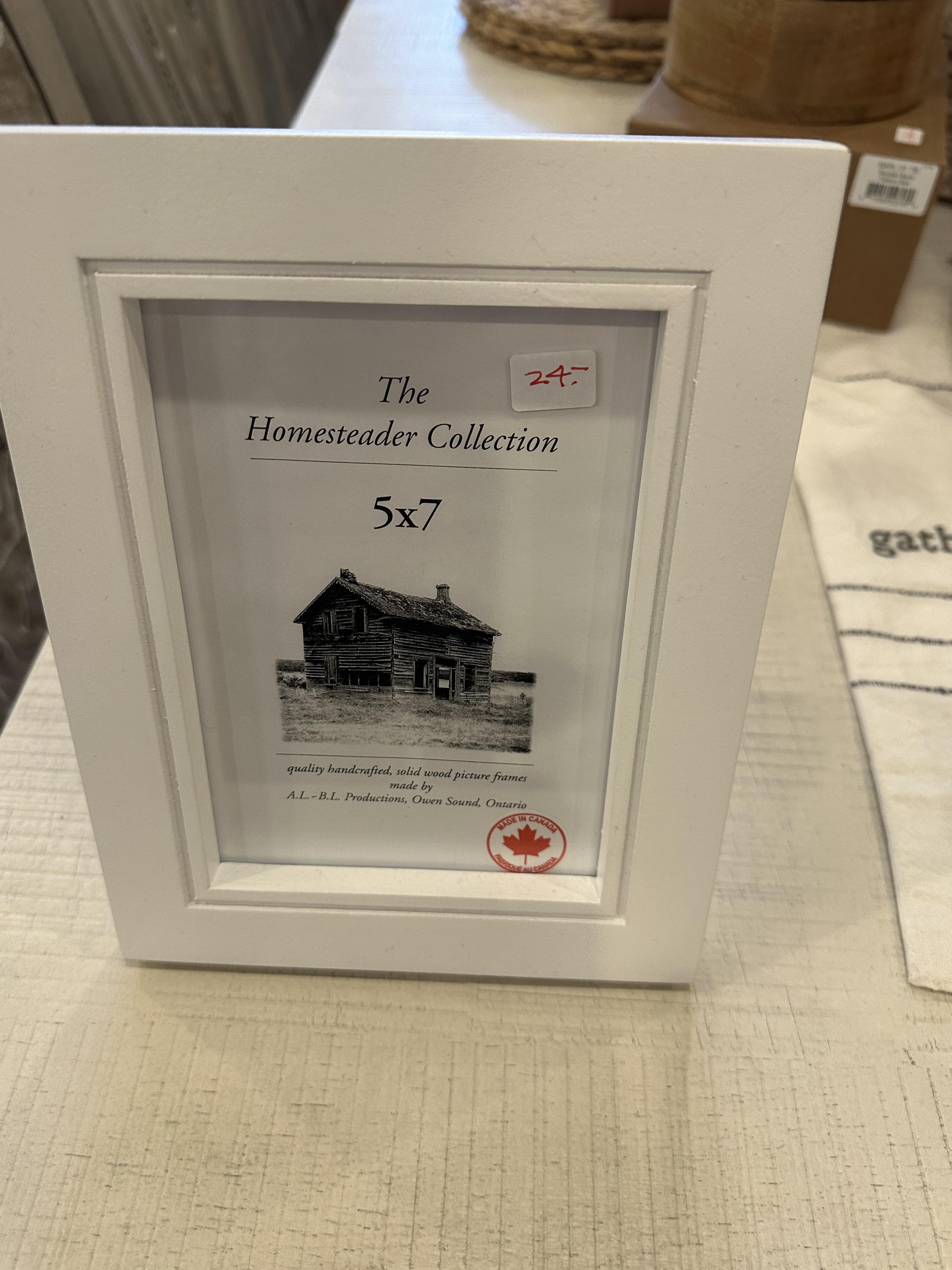 White wooden picture frame with a glass front and a label for The Homesteader Collection. 