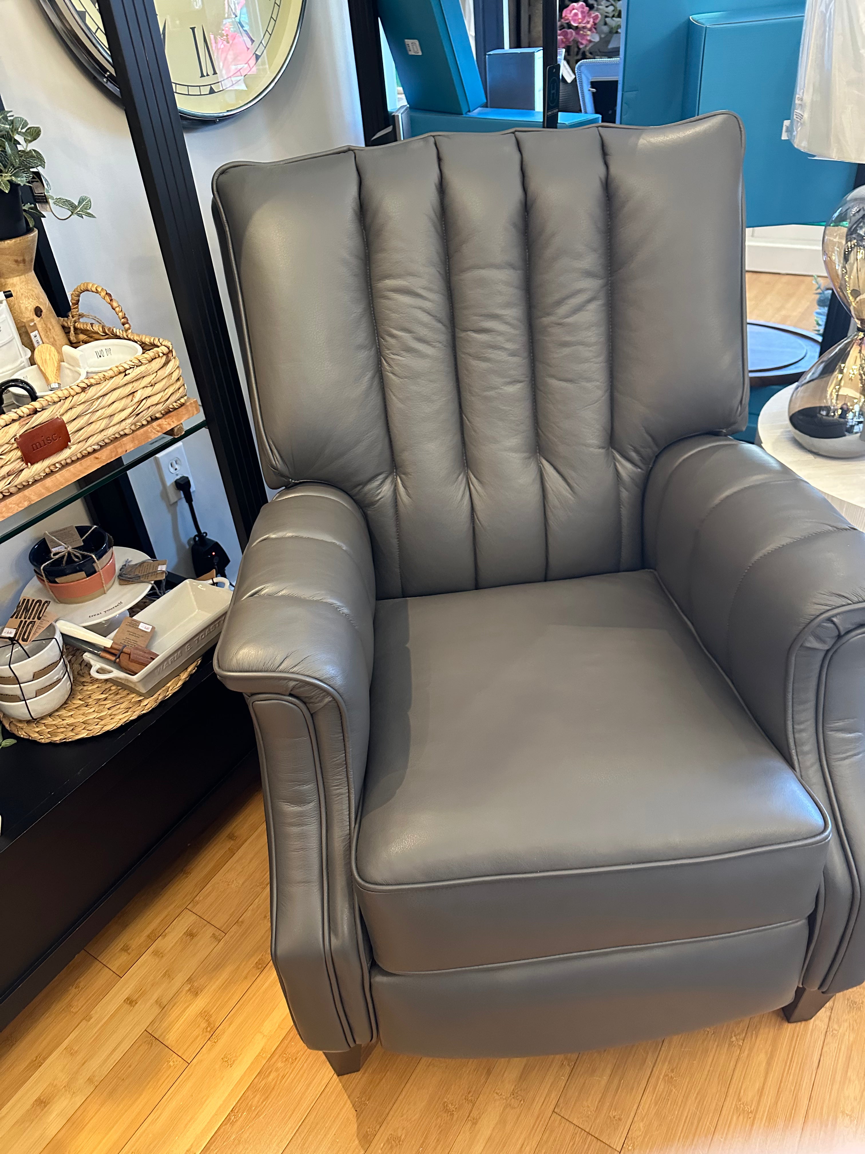 A gray leather reclining chair with high backrest and armrests, displayed in a room setting.