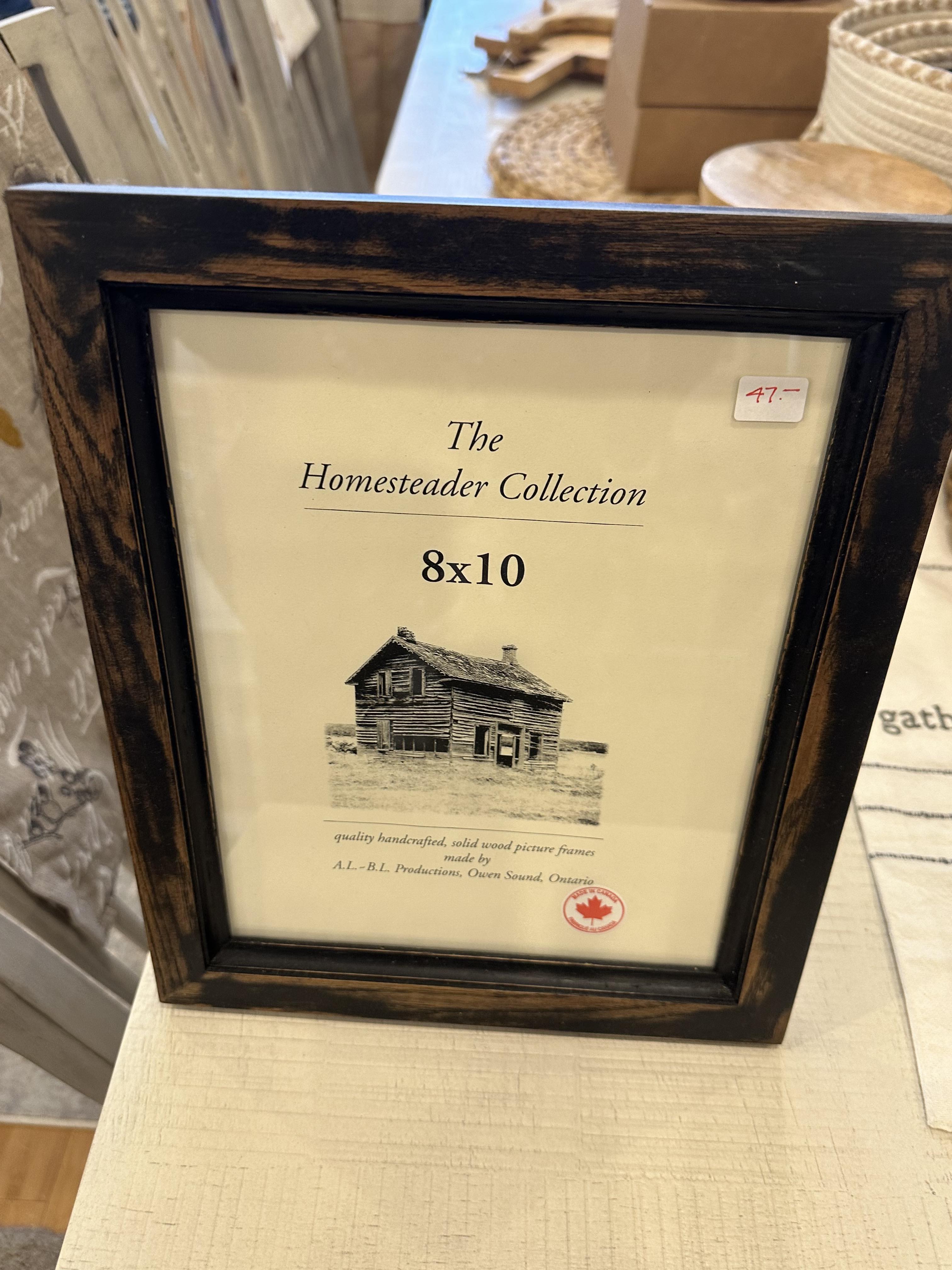 An 8x10 picture frame with a black distressed finish, a clear glass panel, and a wooden border, labeled as 'The Homestead Collection'.