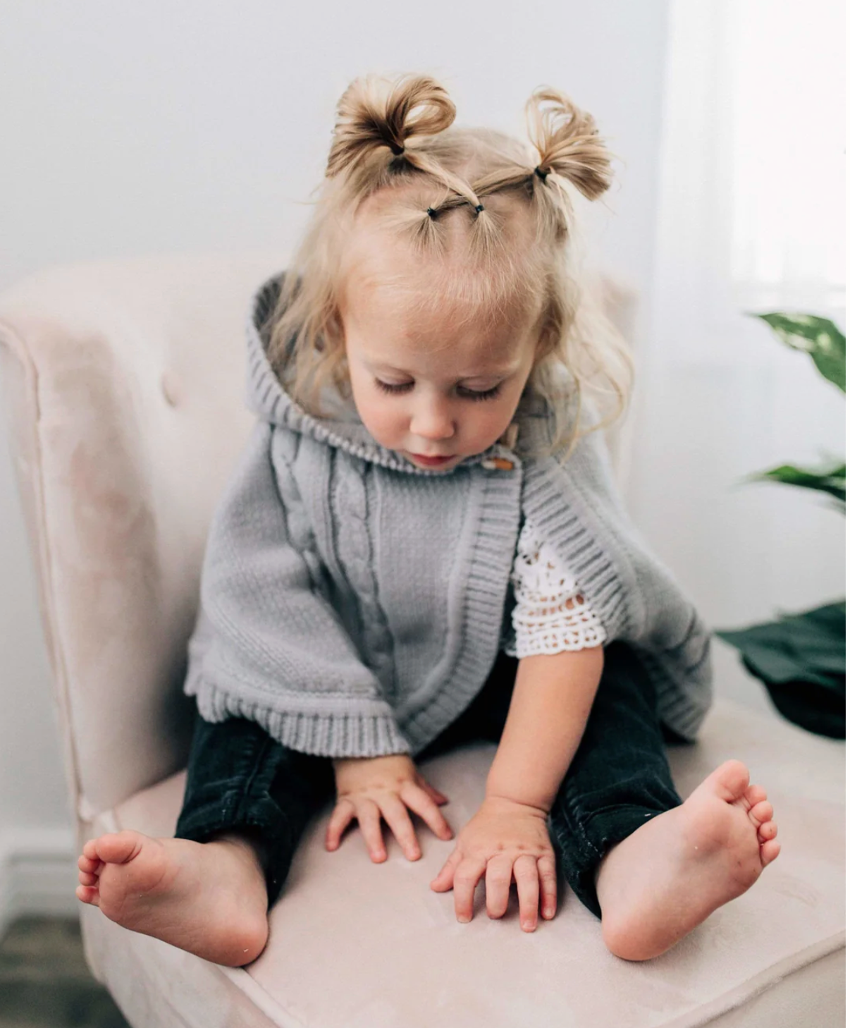 Child wearing a gray knit poncho sitting on a white chair