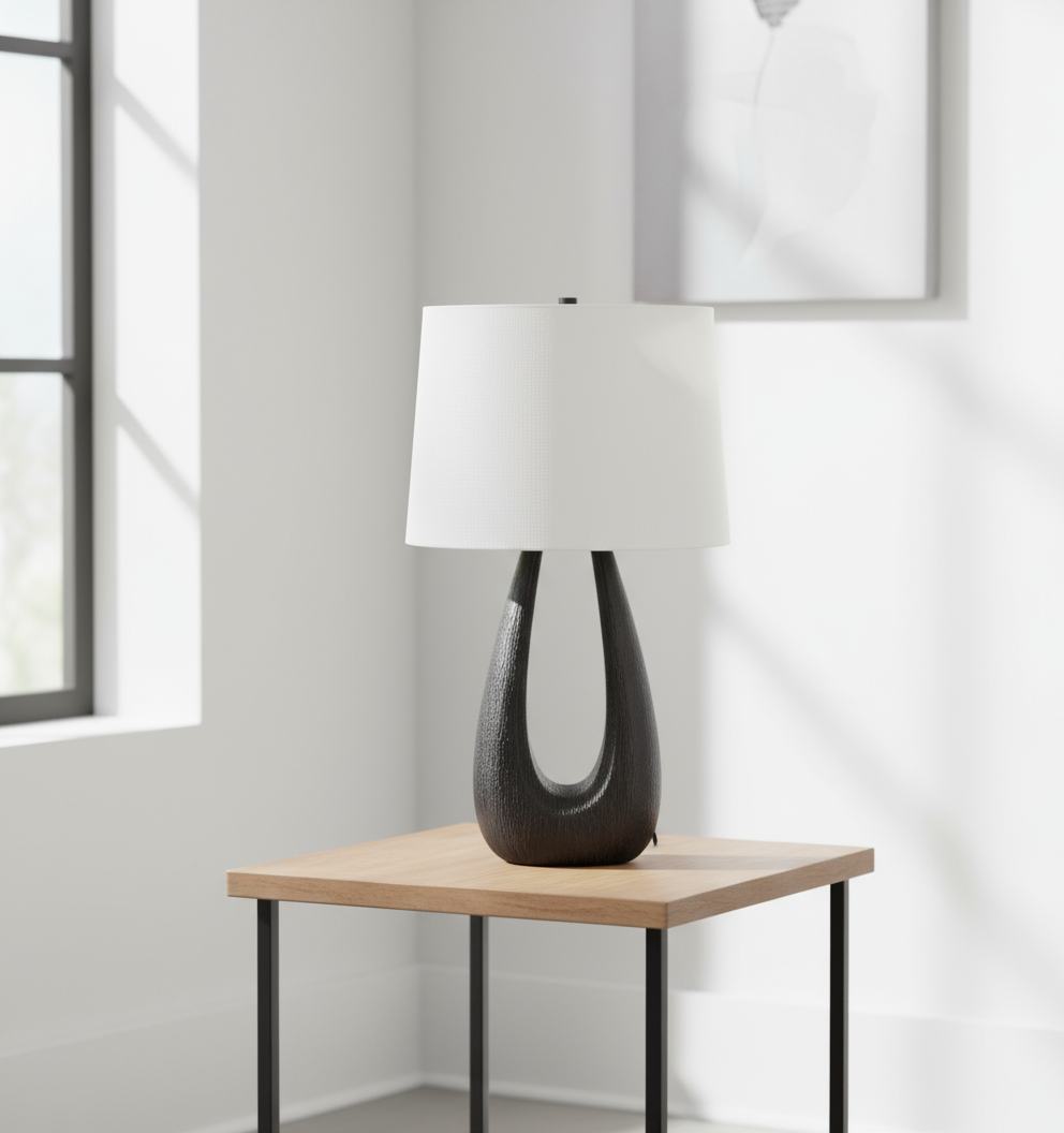 Table lamp with a black base and white shade on a wooden side table in a room with a window.