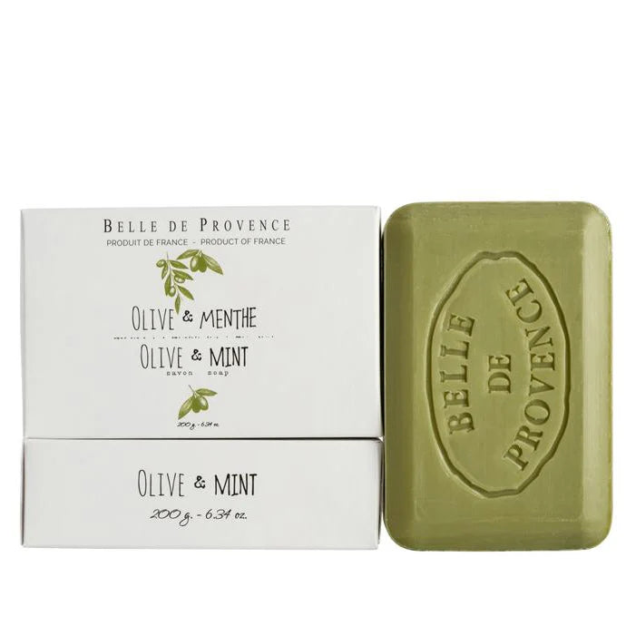 White package of Belle De Provence Olive & Mint hand soap beside a green bar of soap on a white background. 
