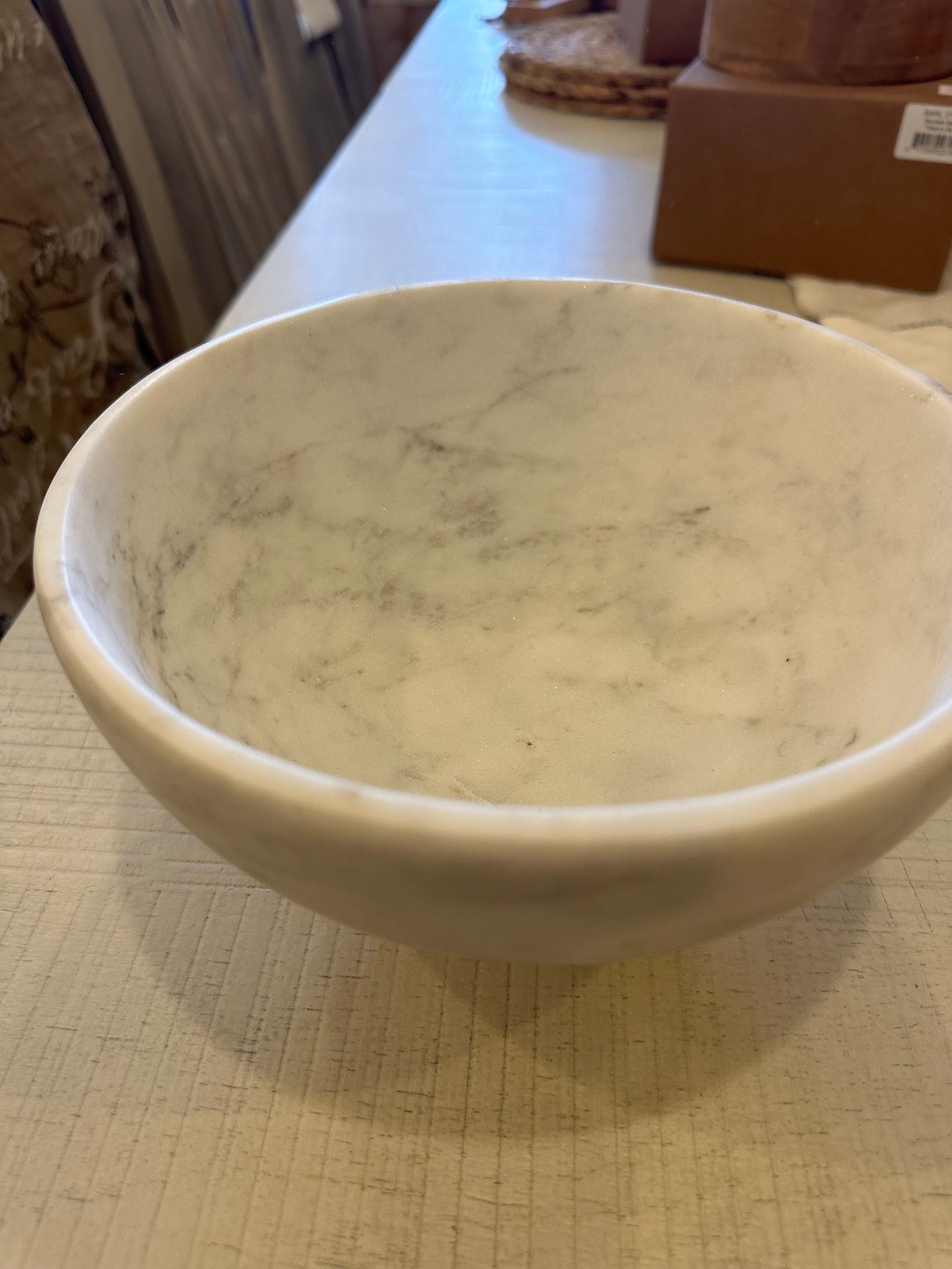 This image displays a classic marble bowl, featuring a smooth, glossy finish with a subtle swirling pattern that adds texture and depth to its surface. The bowl sits on a wooden table, which complements its natural, organic color.