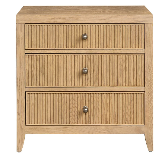 A beige wooden three-drawer nightstand with vertical indentation detailing on each drawer and metal ring pulls.