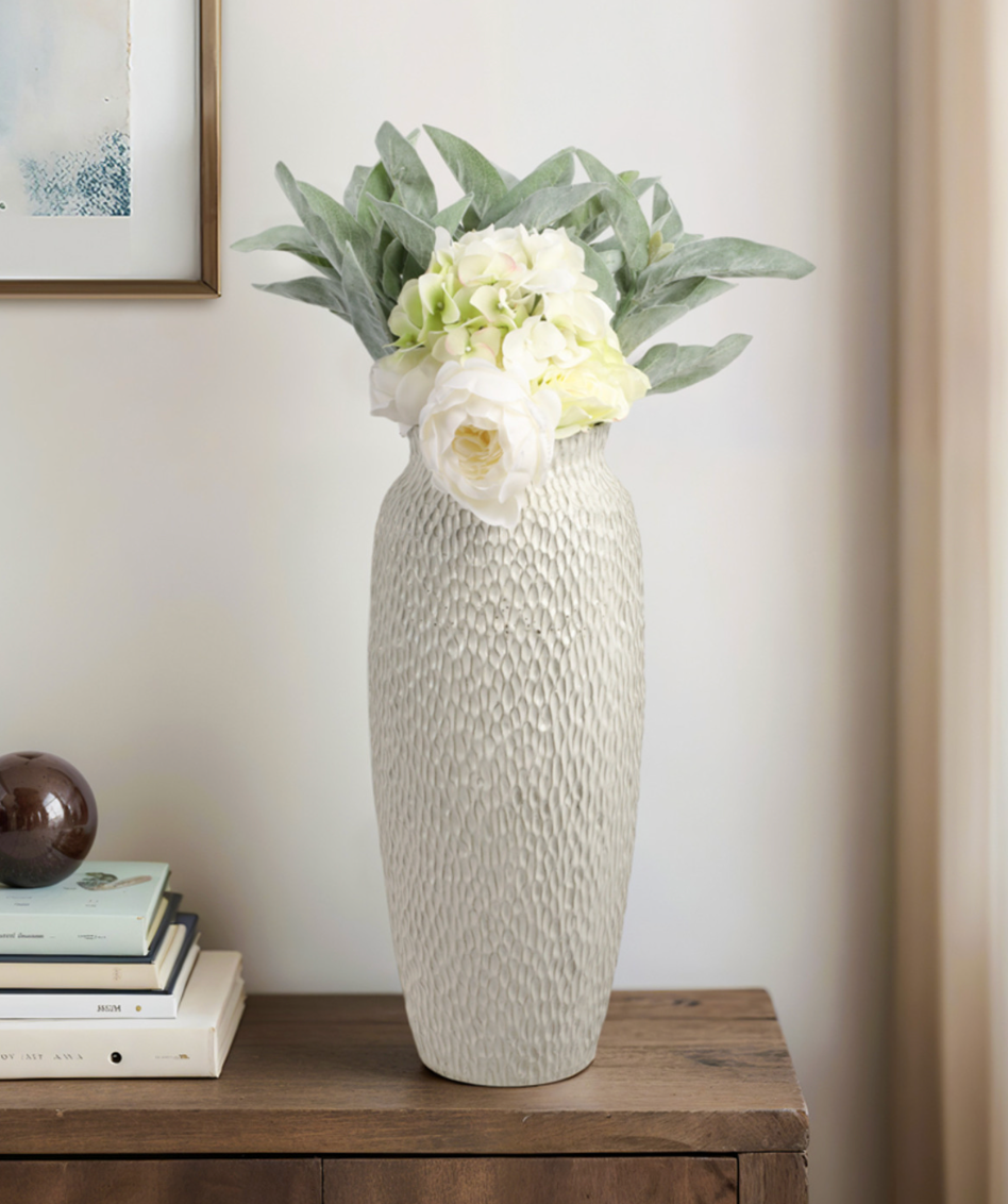 Decorative vase with flowers on a wooden surface against a neutral wall.