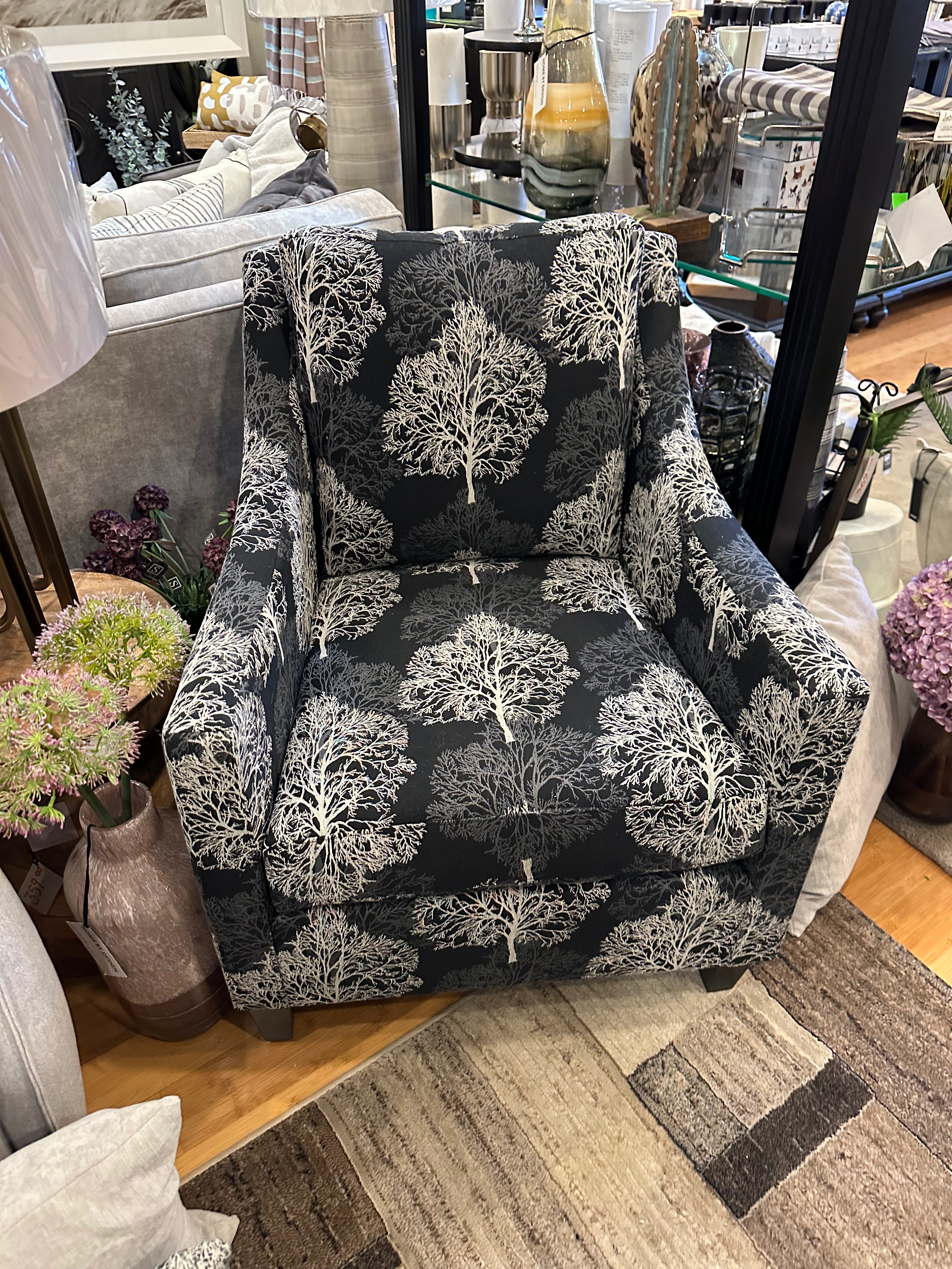 A chair with a floral pattern in black and white colors, positioned in a room setting with decorative items around it.