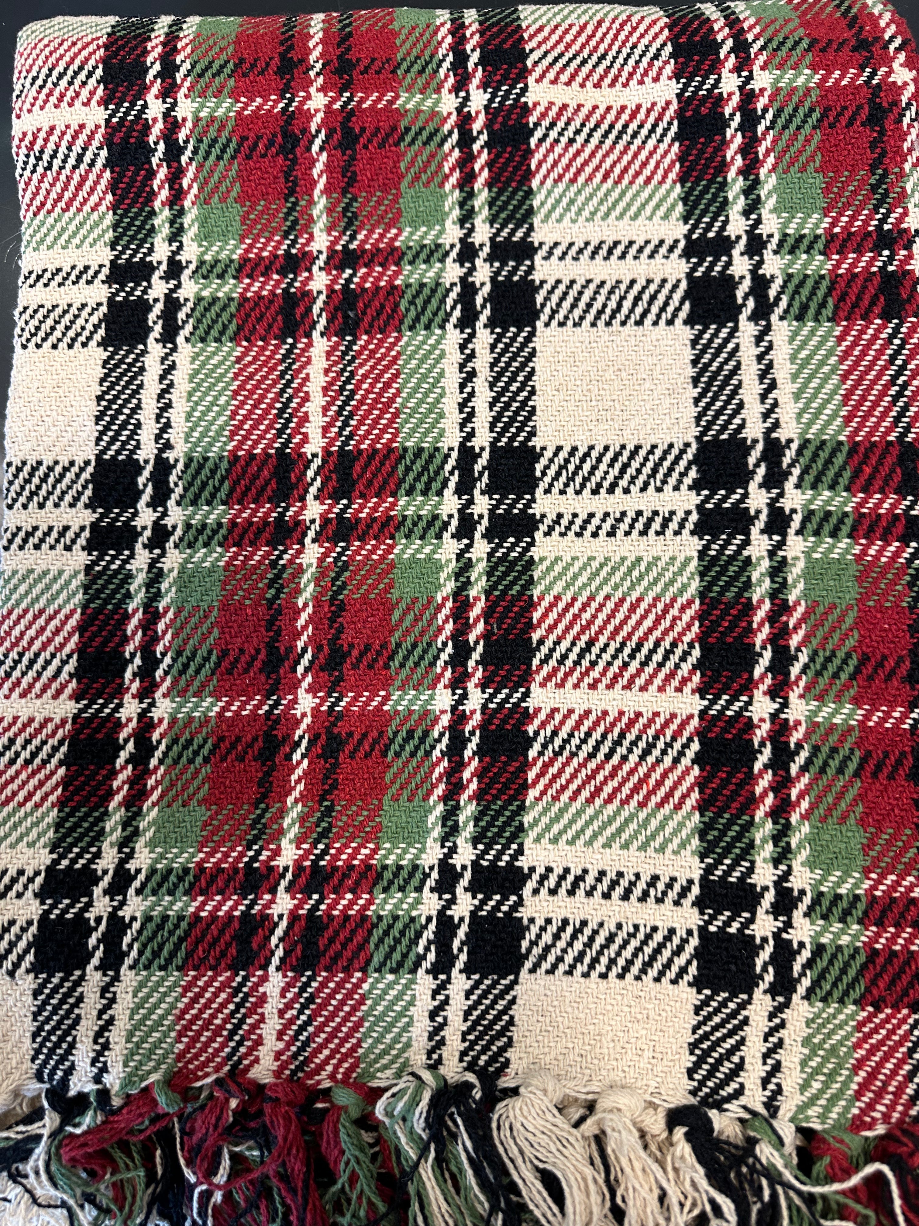 A cream, red, and black plaid throw blanket with a fringed edge.