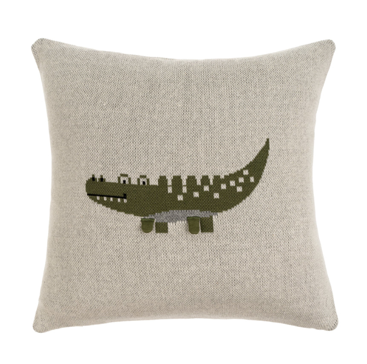 A knit pillow with a crocodile pattern in green and beige colors on a light background.