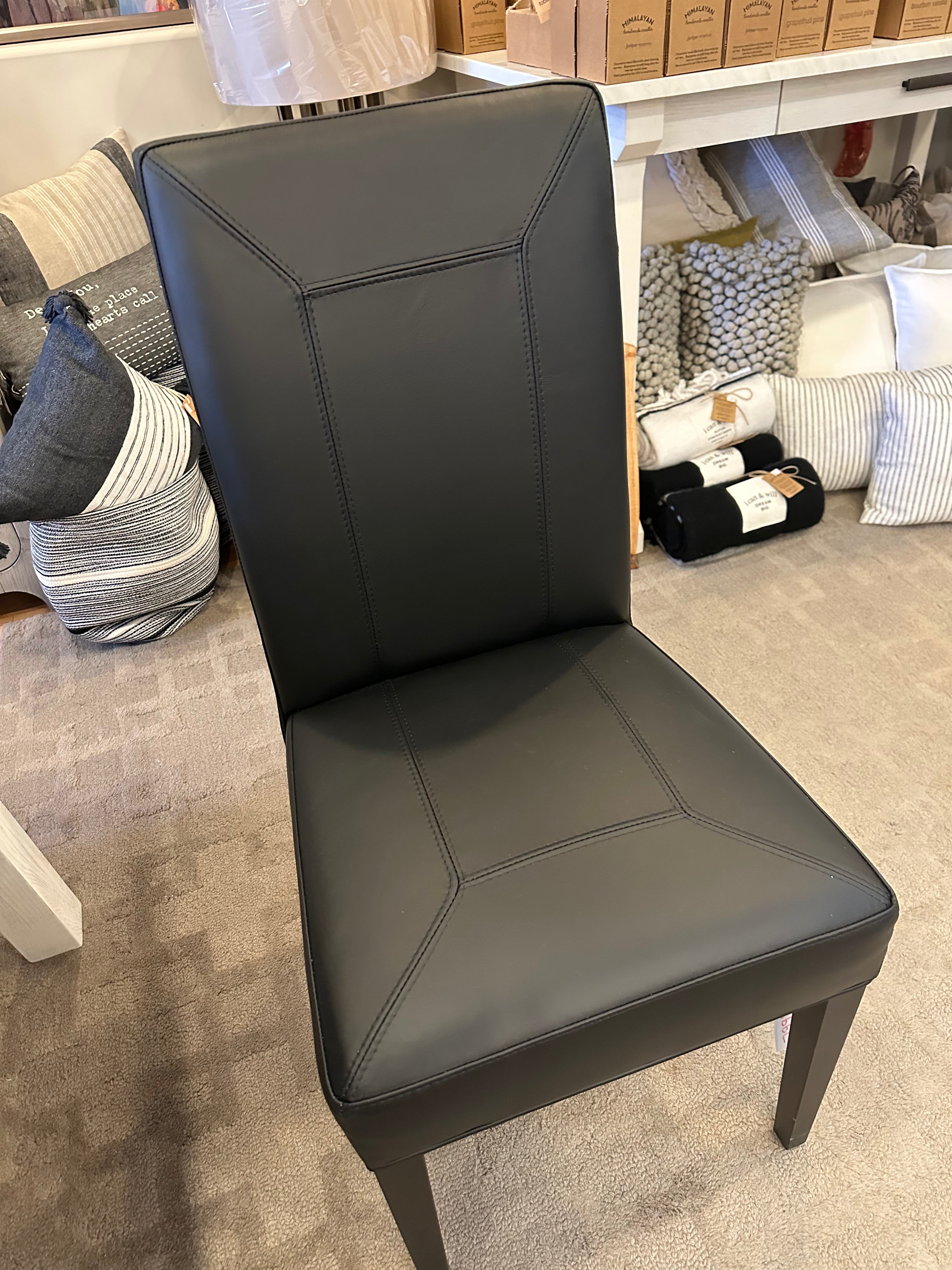 A black upholstered dining chair with a contemporary design, featuring a high back and a seat cushion, displayed in a furniture setting.