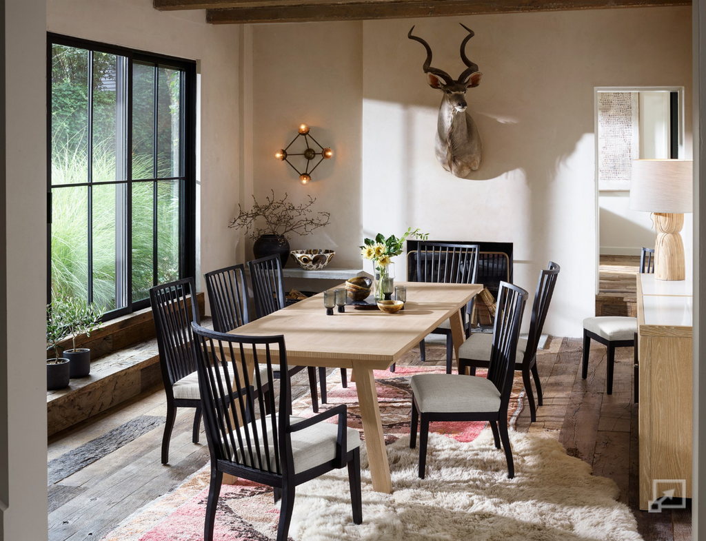 Dining room with wooden table and black chairs, large window, and decorative antlers on the wall.