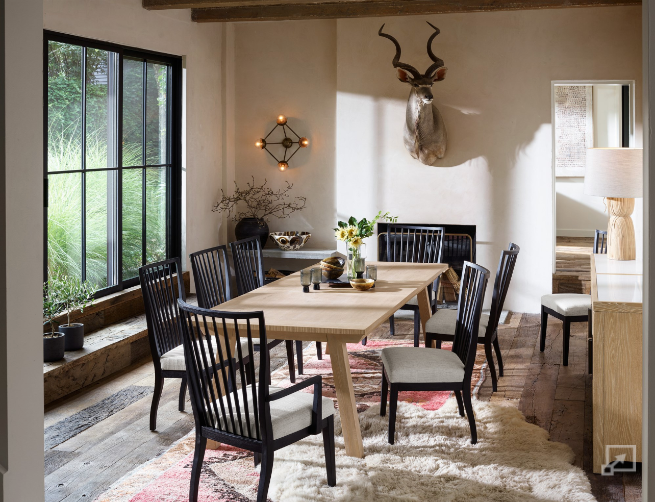 Dining room with wooden table and black chairs, large window, and decorative antlers on the wall.