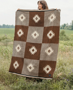 Person holding a large brown and gray patterned blanket in a field