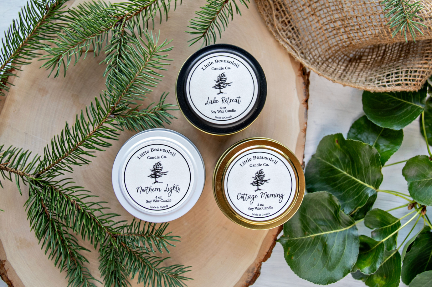Three candles with labels on a wooden surface with greenery