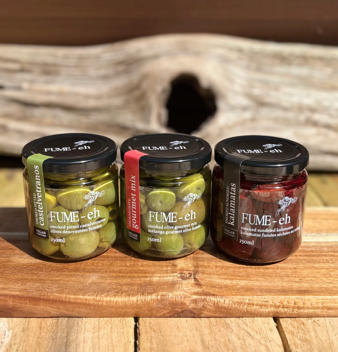 Three jars of FUME-eh olive products on a wooden surface with a rustic background.