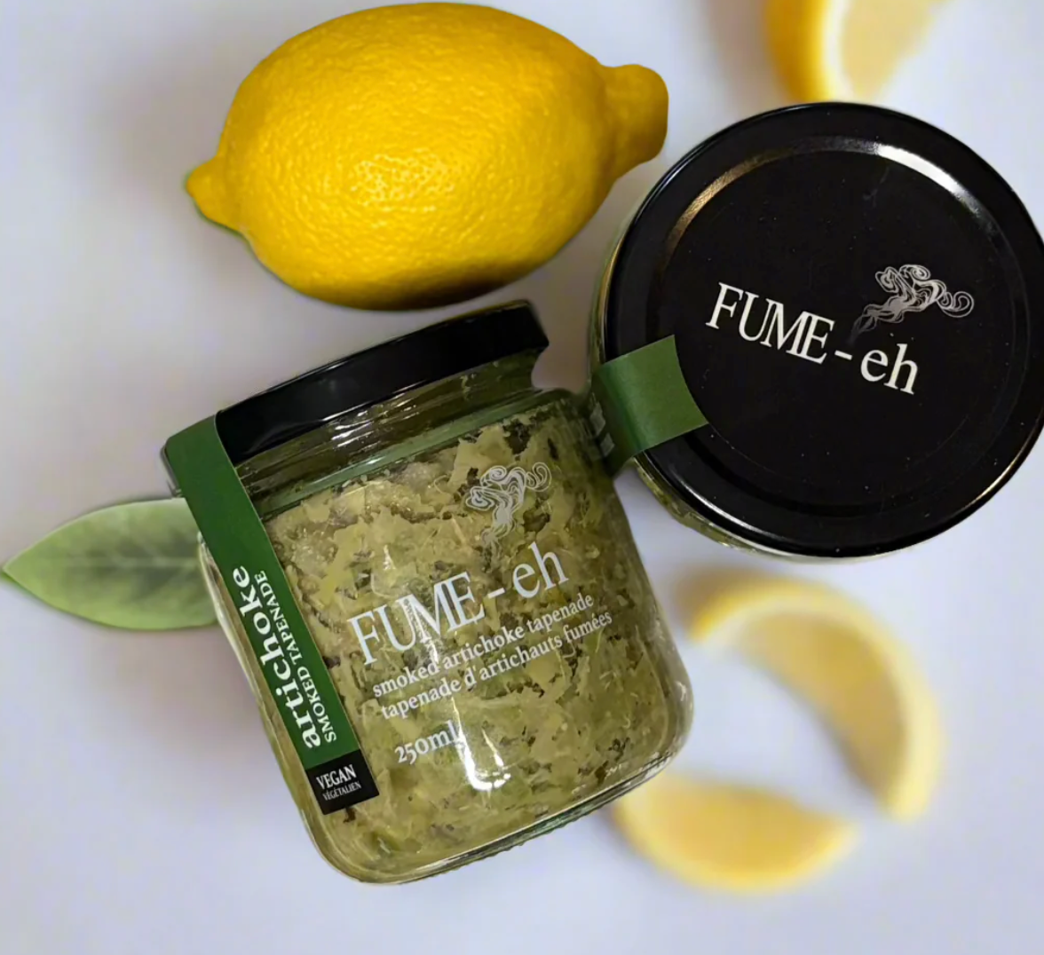 Jar of FUME-eh smoked artichoke tapenade with a lemon and leaves on a white background