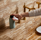 Person applying soap to a bar of soap on a marble countertop with gold fixtures.