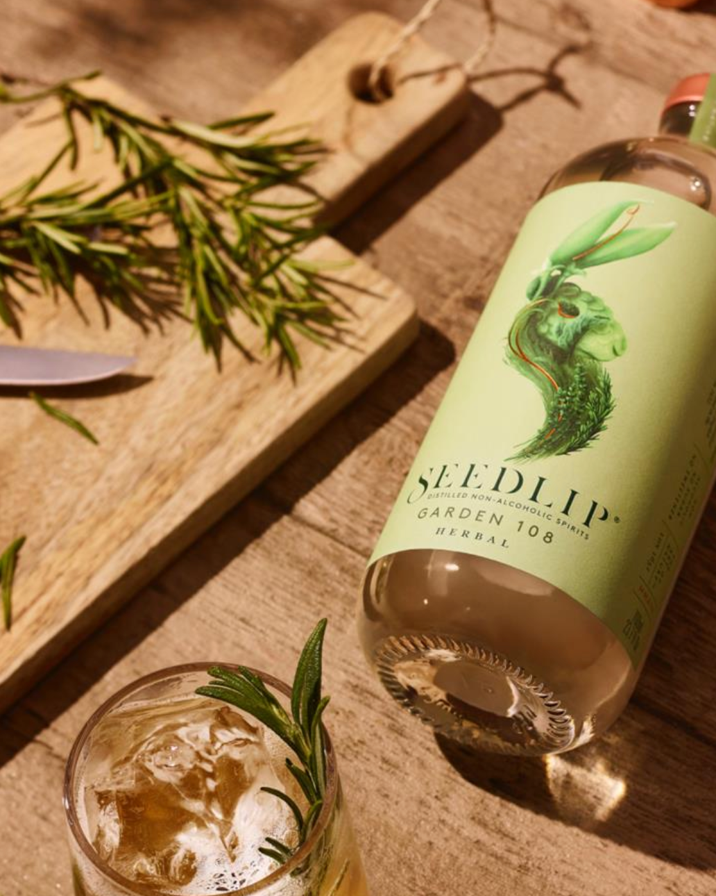 Bottle of Seedlip Garden 108 Herbal and glass on a wooden surface with herbs