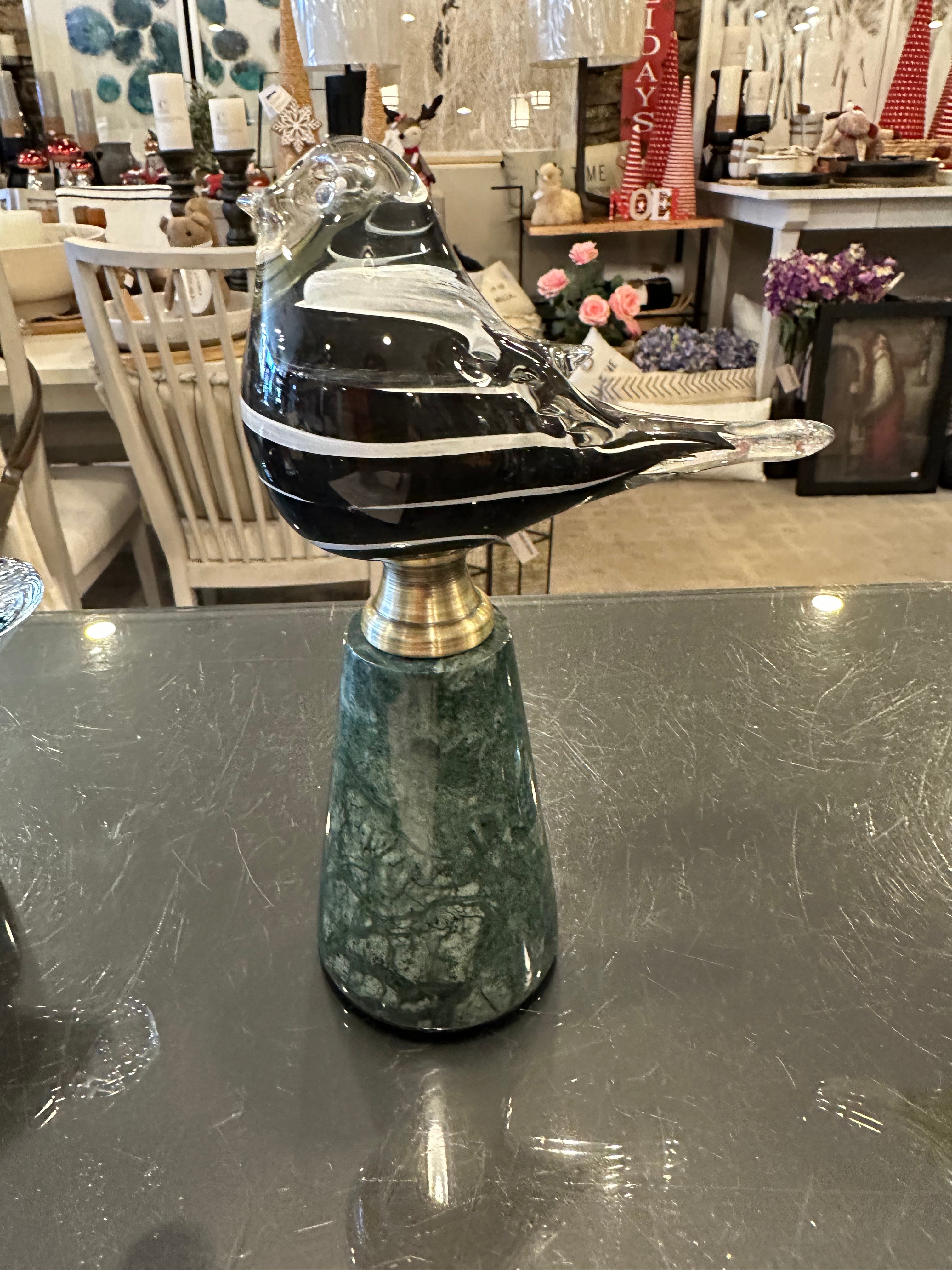 Glass black and white bird perched on a green marble pedestal with gold accent. 