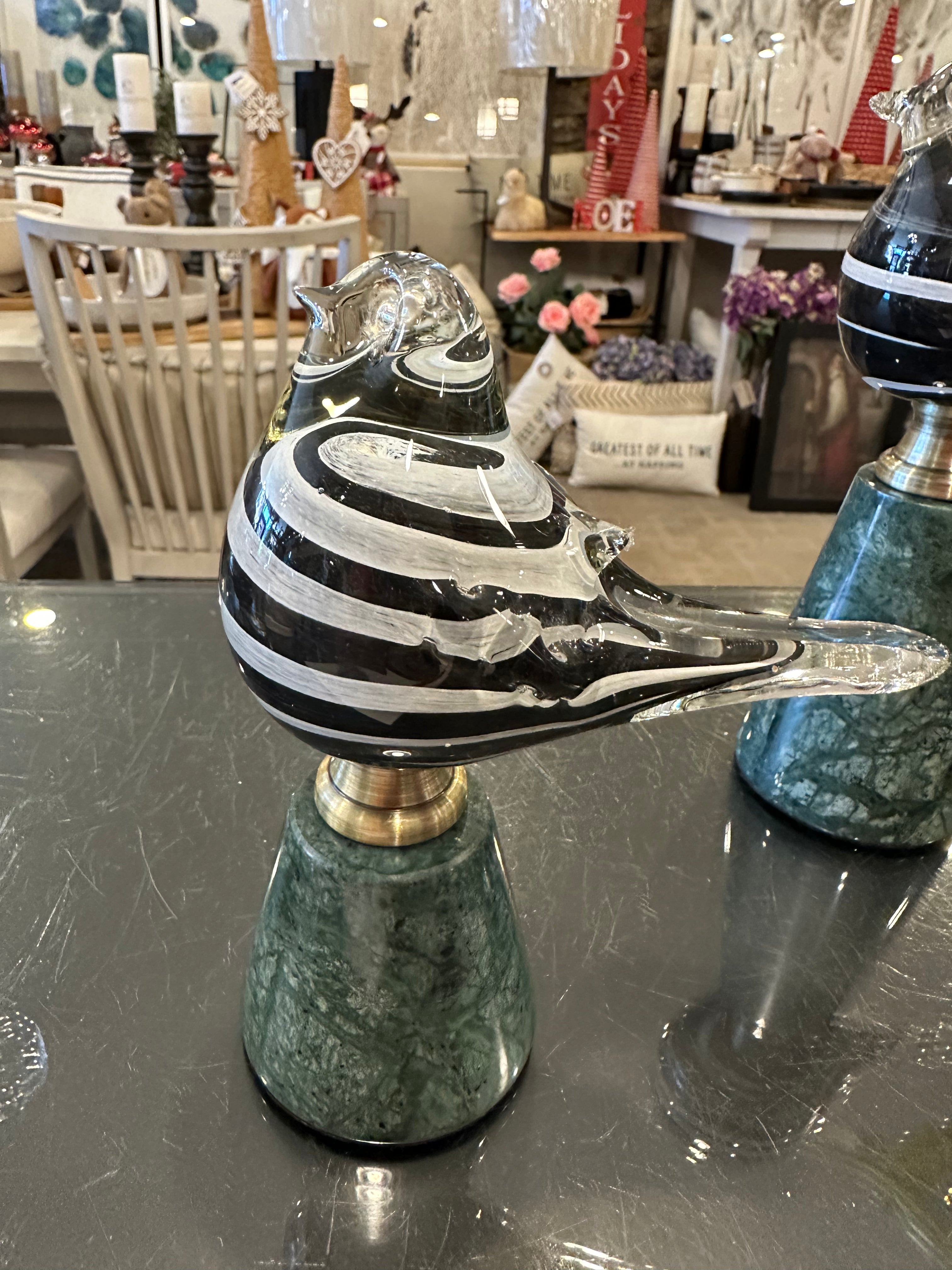 A glass figurine of a bird perched on a marble stand, with a black and white striped pattern.