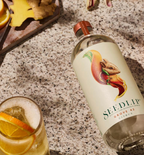 Bottle of Citrus Grove 42 Seedlip beside a fizzy cocktail with an orange slice. 