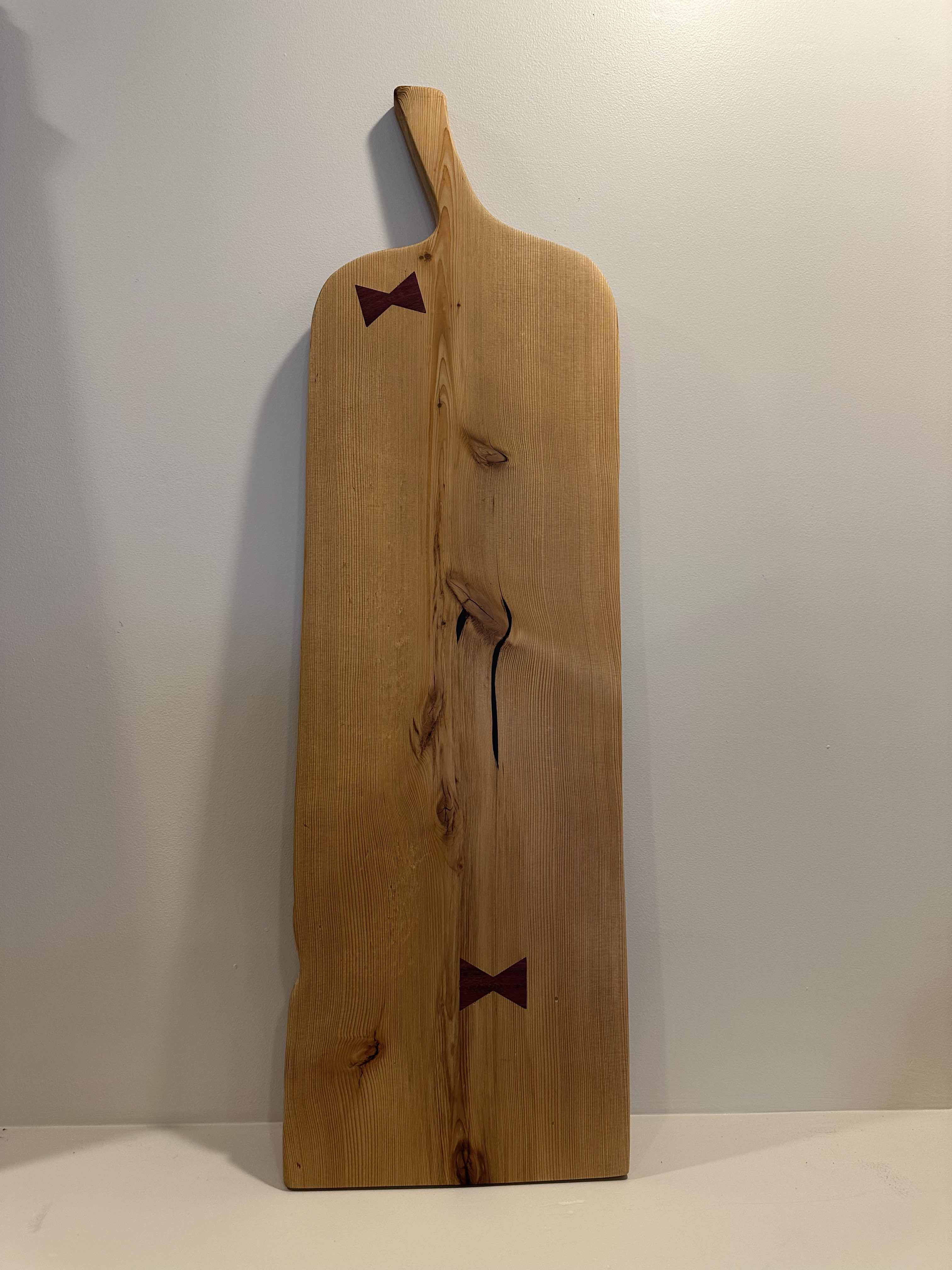 A large, natural wooden serving board with a smooth finish and a small decorative bow on it, displayed against a white background.