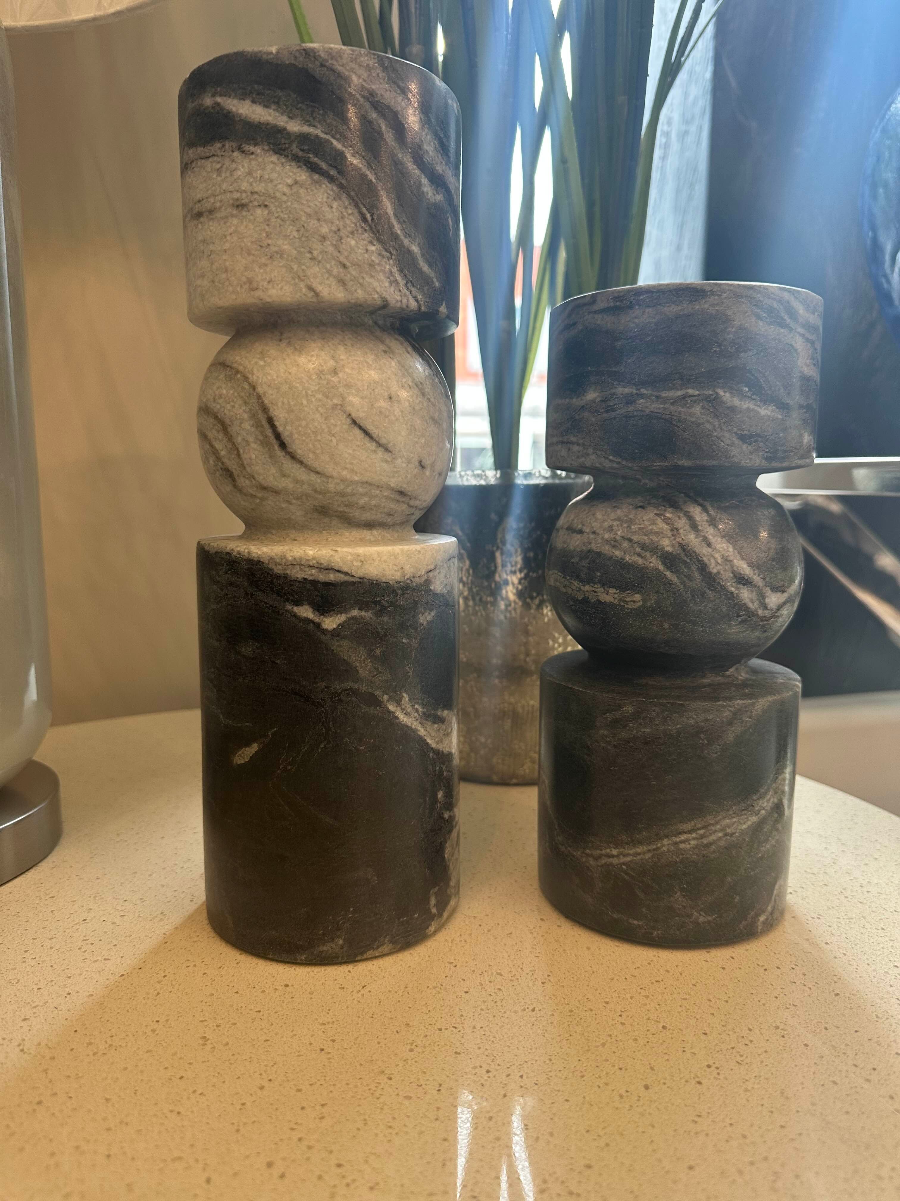 Stacked black marbled stone candle sticks on a reflective surface with a blurred background