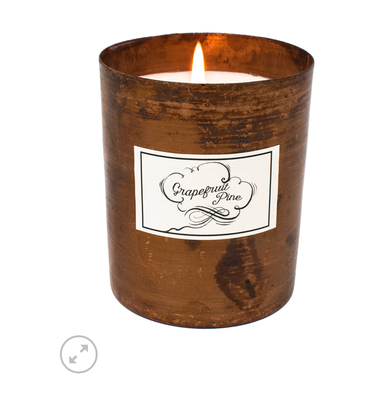 A sleek metal  tumbler candle with a blackened patina finish, featuring a label with 'Grapefruit Pine' written on it.