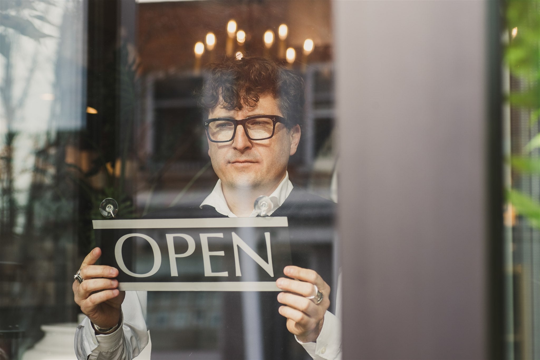 Man holding an 'OPEN' sign behind a glass door