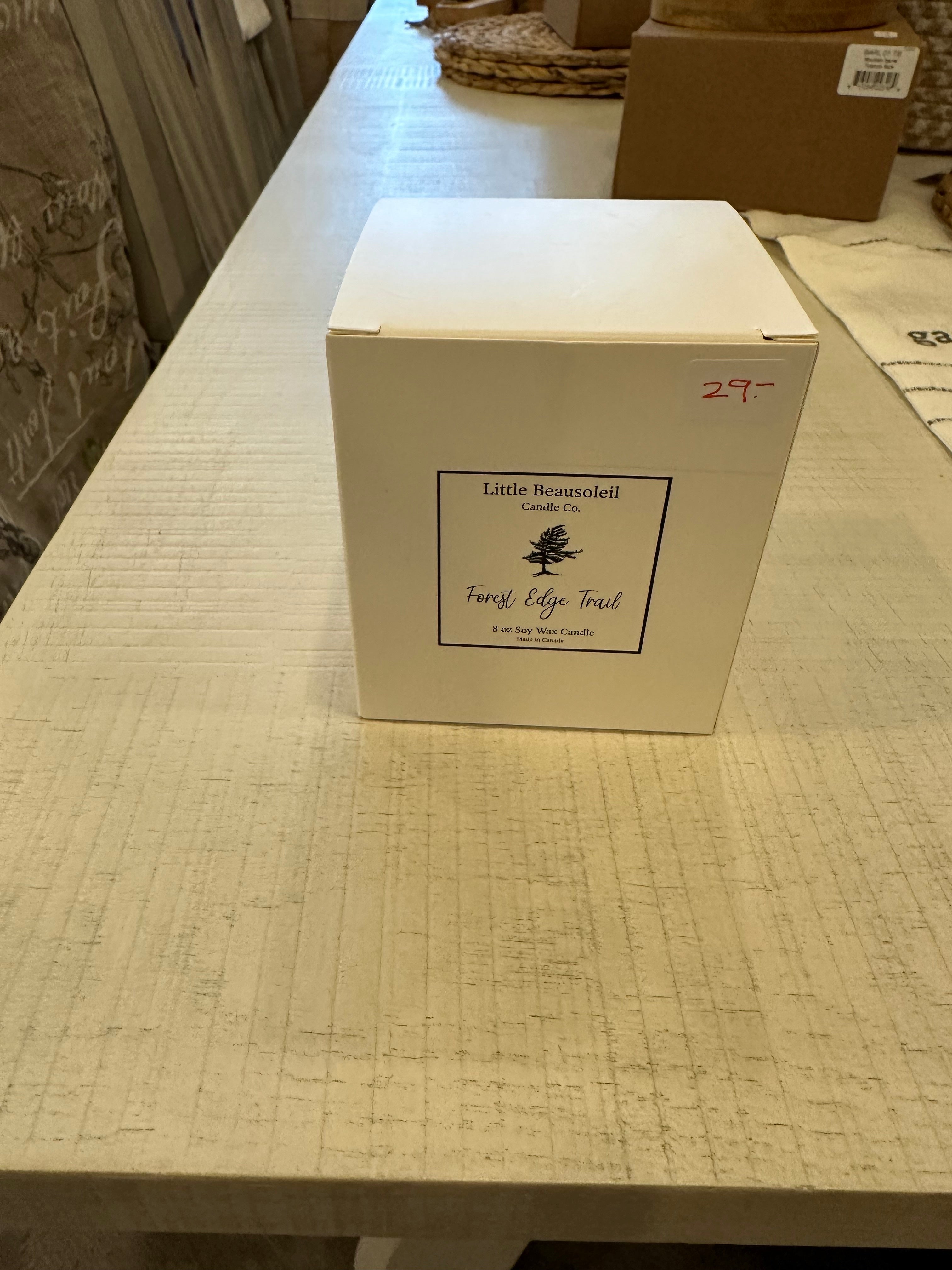 A white jar candle labeled 'Little Beausoleil Forest Edge Trail' placed on a wooden surface.