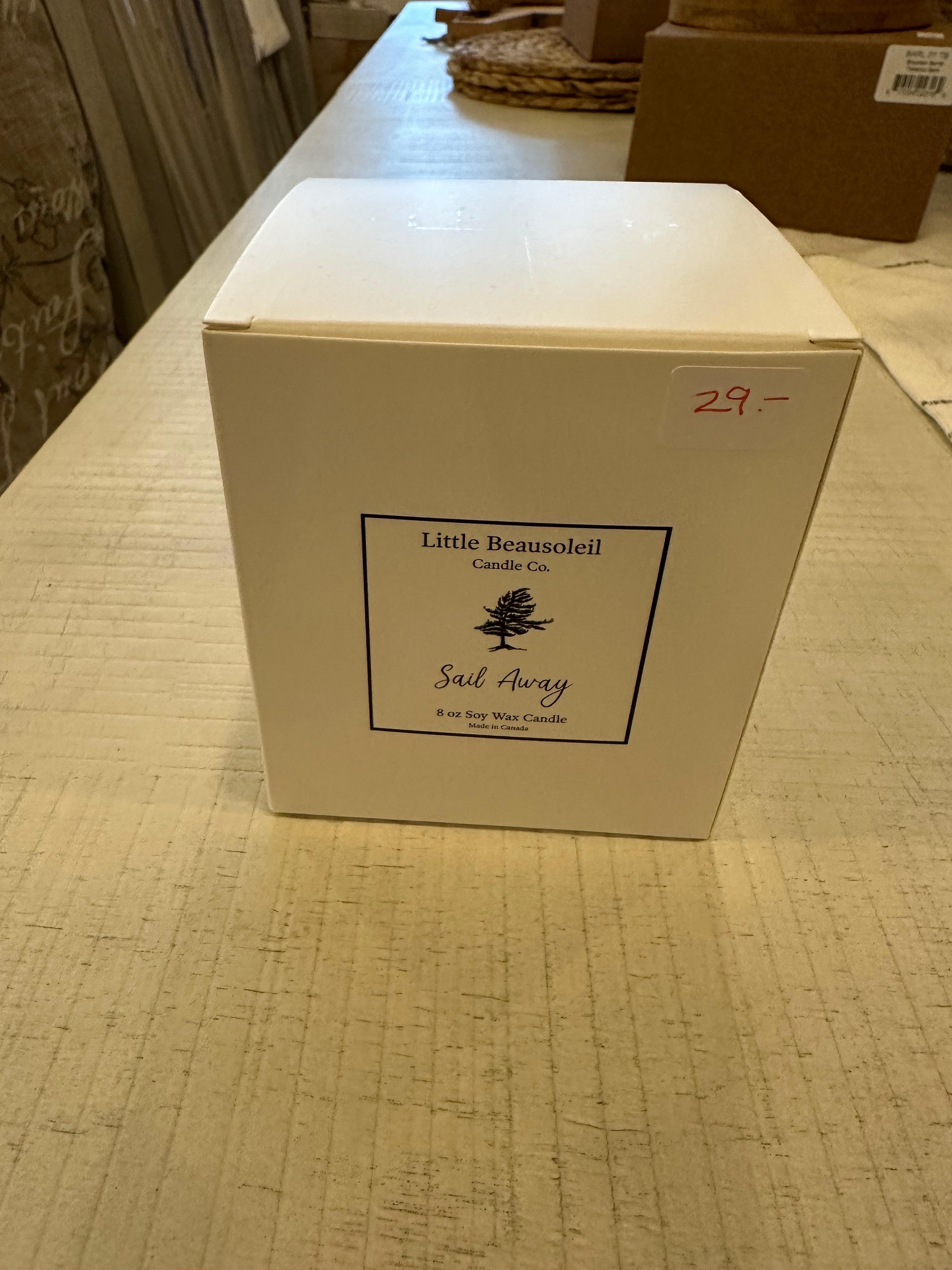 A white jar candle with a label that reads 'Little Beausoleil Candle Co Sail Away' placed on a wooden surface.