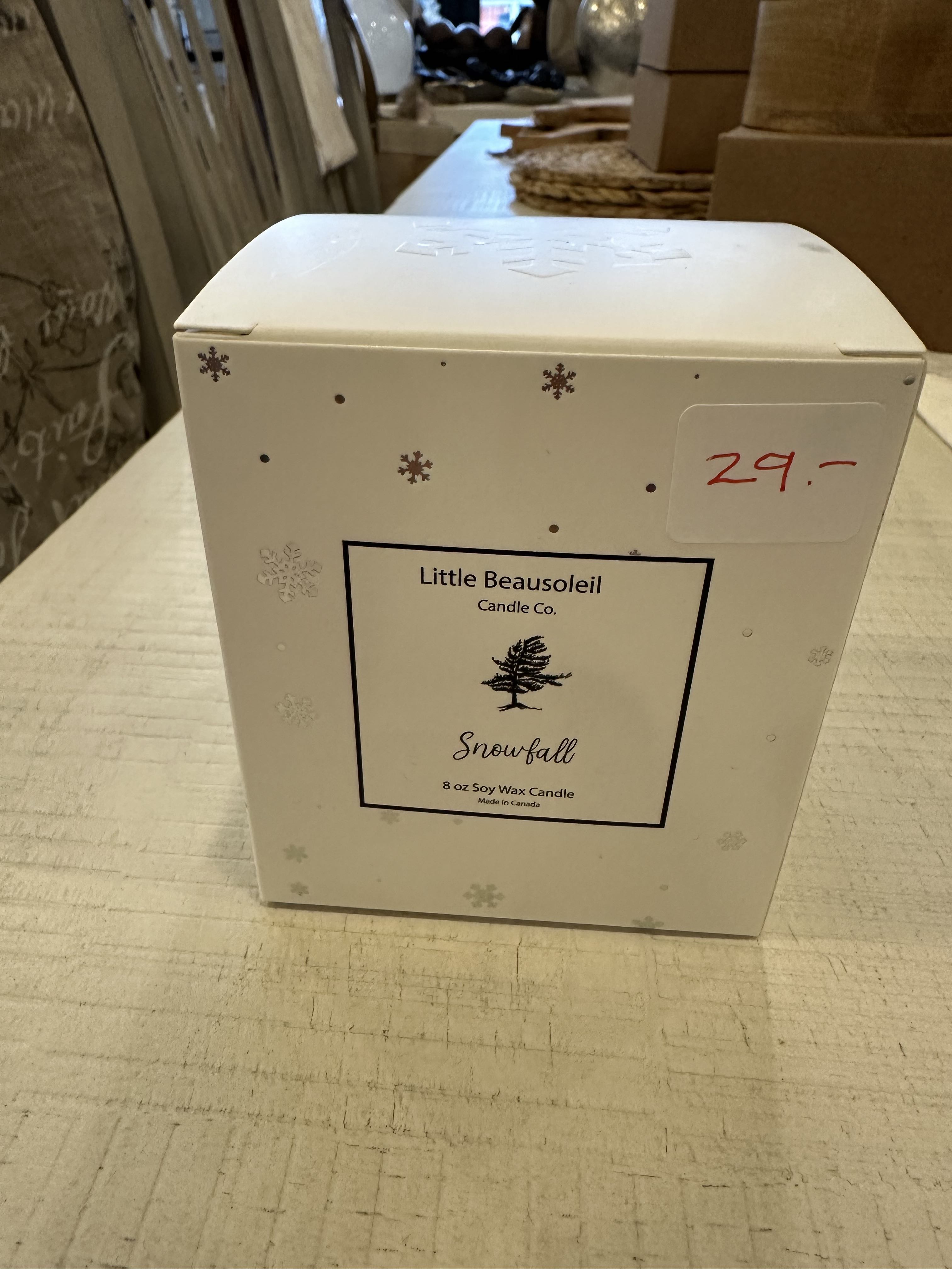 A white jar candle with a label that reads 'Little Beausoleil Snowfall', with a price tag of $29 on it, displayed on a table.