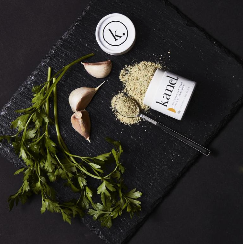 Black slate cutting board with garlic and parsley and a tipped over cainnister of Kanel Holy Grail Garlic Sale. 