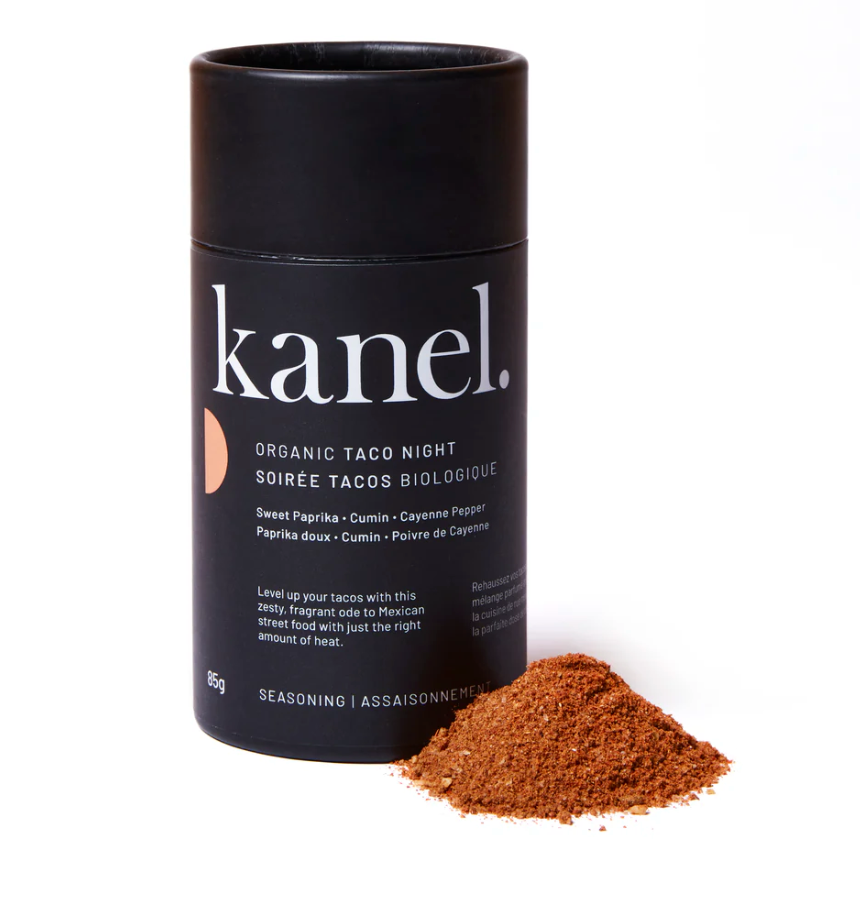 Black cylindrical cannister of Kanel organic taco night seasoning on a white background with a small pile of red seasoning. 