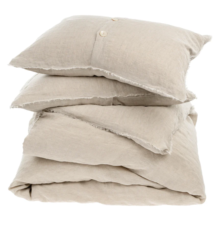 A stack of beige chambray linen duvet covers and pillowcases with frayed edges and button closures.