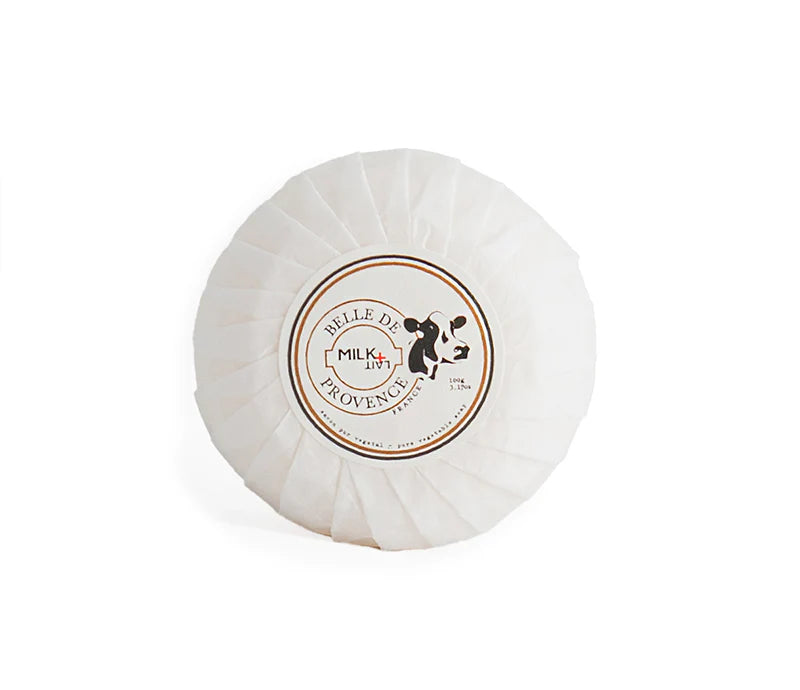 A round soap wrapped in white paper with the label "Belle De Provence - Milk" with an image of a cow. 