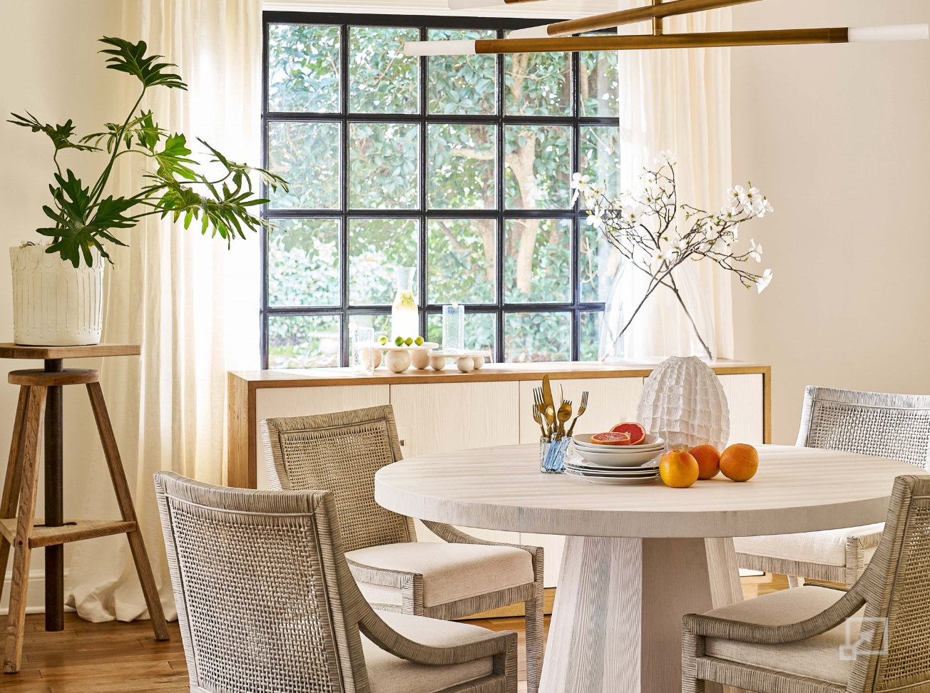 Dining room with a round table and chairs, plants, and a large window.