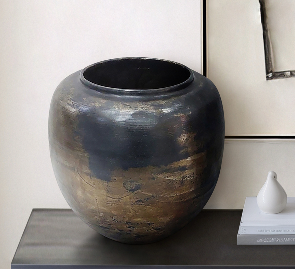 Black ceramic pot with bronze detail on a side table.
