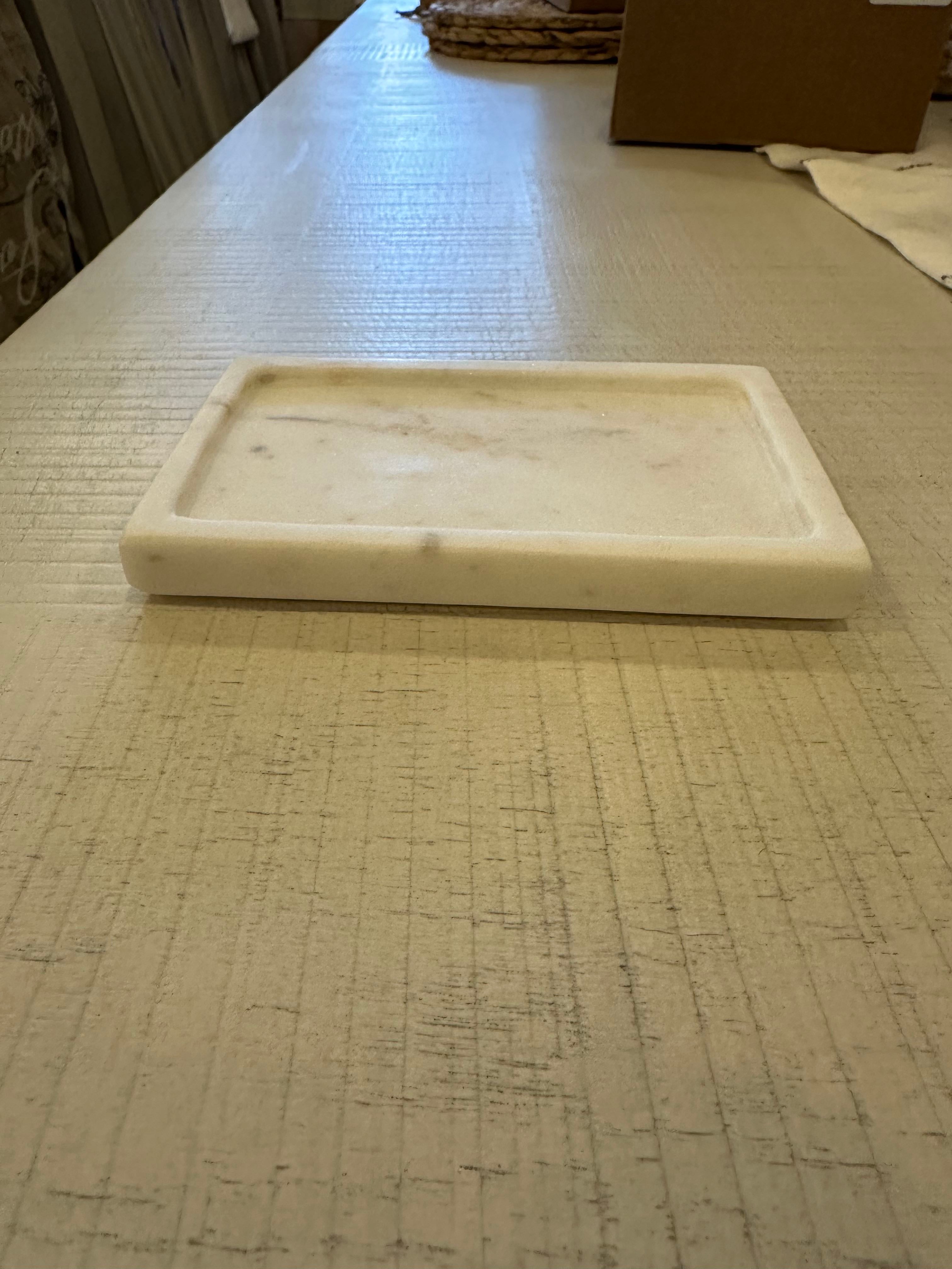 A white marble soap dish placed on a beige surface with a blurred background.