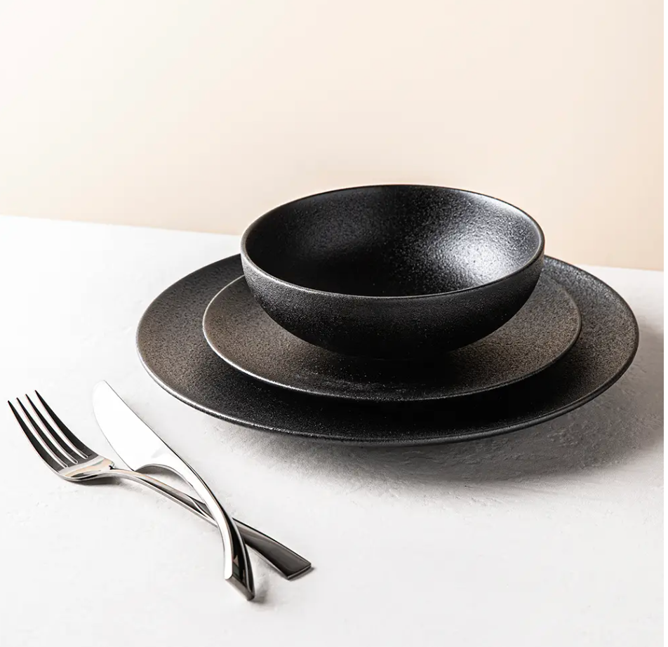 A set of black textured porcelain dinnerware, including a plate and a fork, on a white surface.