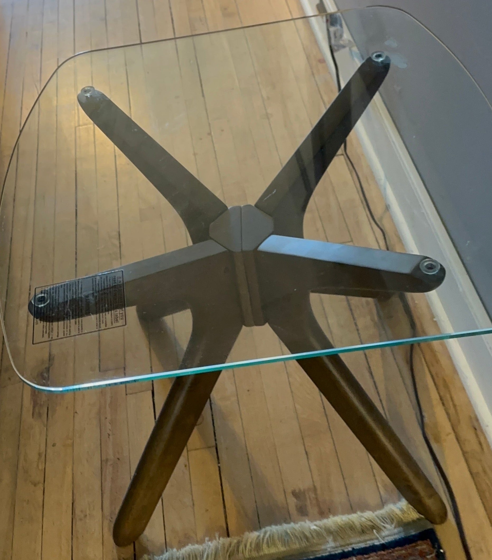 A mid-century modern end table with a clear glass top and a metal frame in brown color, placed on a wooden floor.