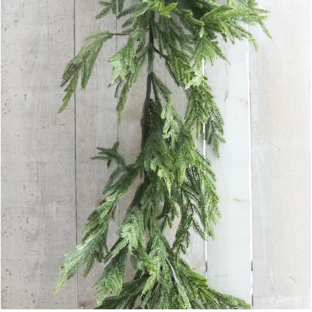 Artificial green garland hanging against a textured light gray wall.