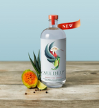 Seedlip Notas de Agave bottle with guava and lime on a wooden surface against a light blue background