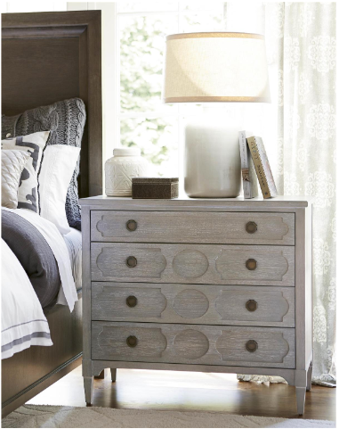A gray chest of drawers with a rustic design, featuring multiple storage compartments and a lamp on top, placed in a bedroom setting.