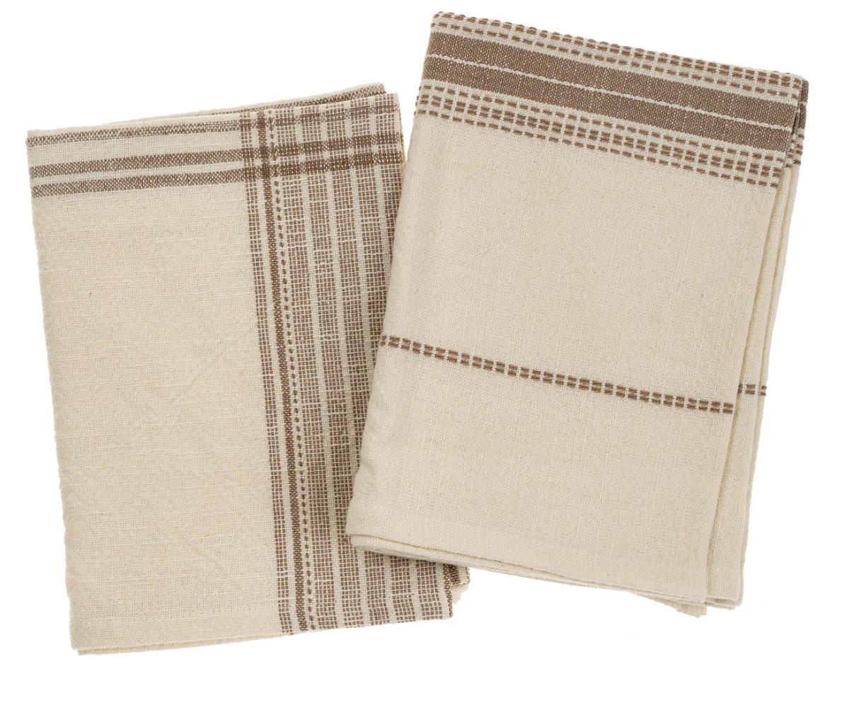 Two folded cotton tea towels with a striped pattern and hand embroidery accents, one in a taupe color and the other in a lighter shade, possibly beige or ecru.