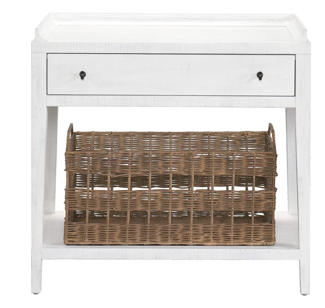A white rustic oak nightstand with one top drawer and a woven open-air storage basket beneath.