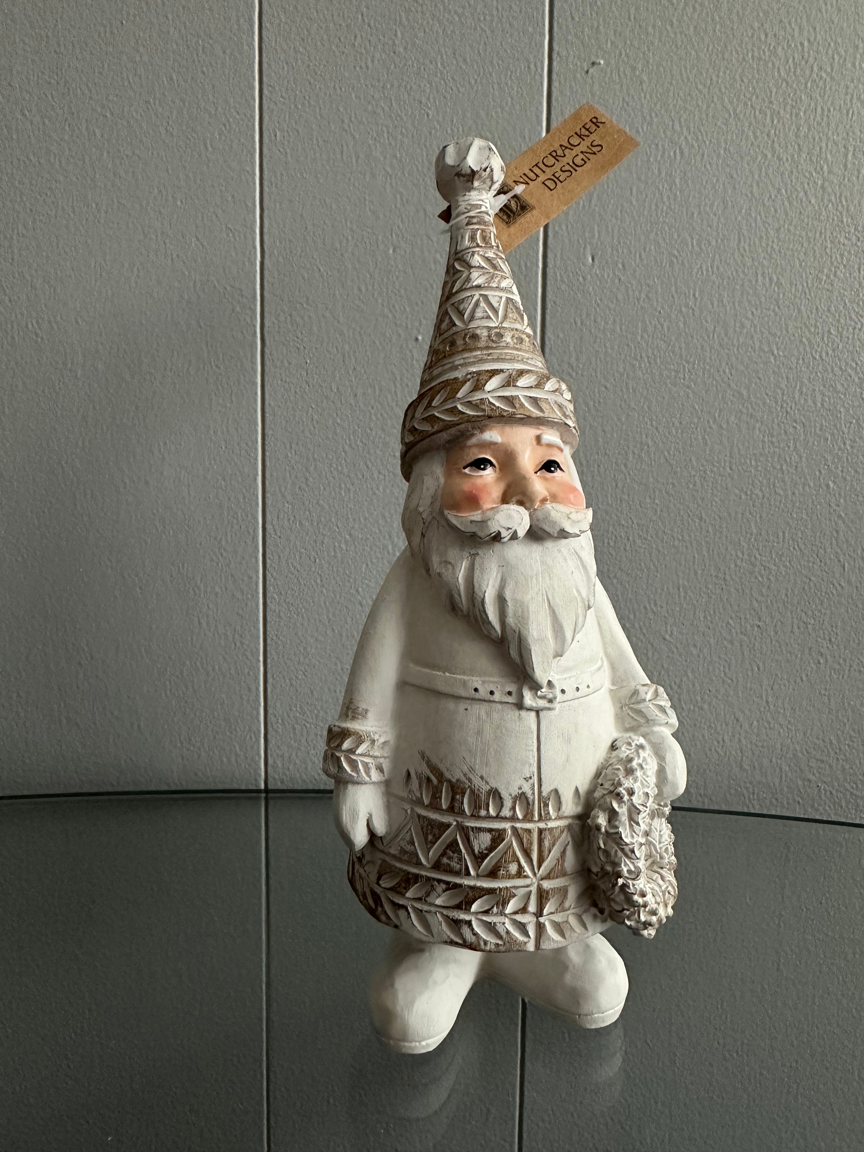 A white ceramic or wooden Santa Claus figure with a beard and a hat, holding a wreath, set against a grey background.