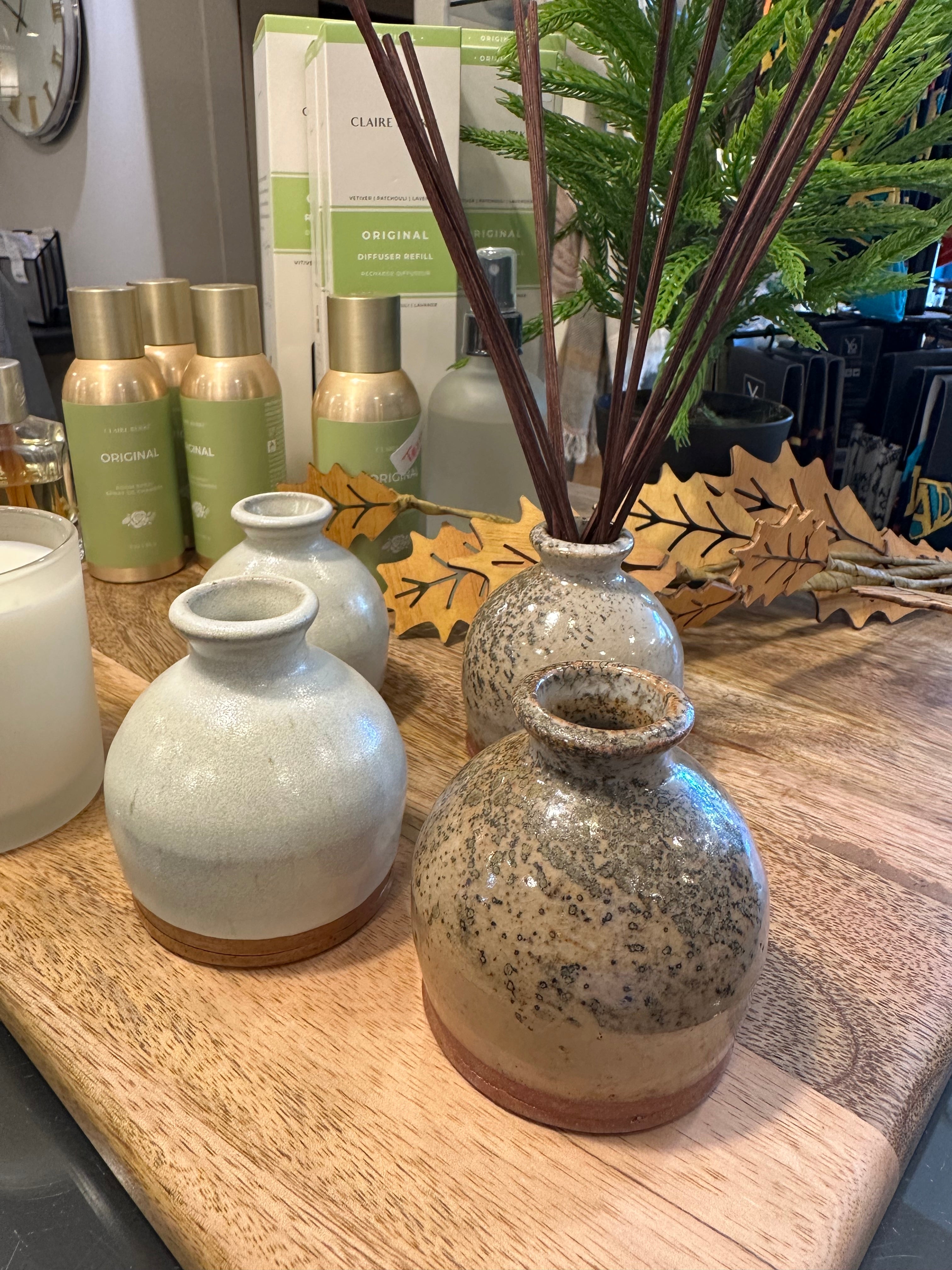 Decorative bud vases on a wooden surface with plants and bottles in the background