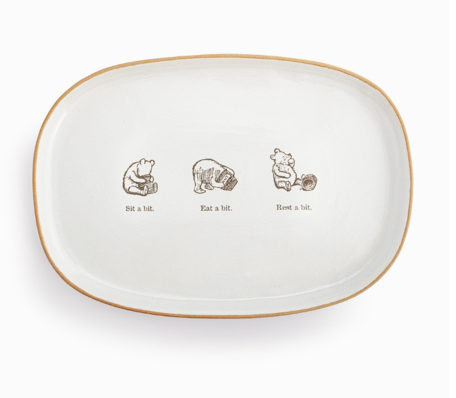 An oval-shaped ceramic platter with illustrations of Winnie-the-Pooh and friends. The platter has a white background with gold trim.